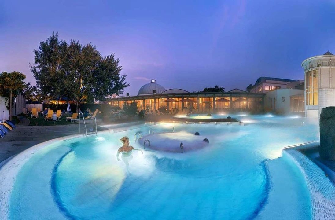 Thermalbad Außenbecken am Abend mit dampfendem Wasser und beleuchtetem Thermengebäude in Süddeutschland