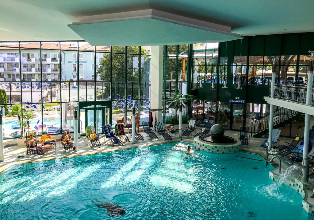 Innenbad der Europatherme Bad Füssing mit türkisblauem Thermalbecken, Liegestühlen und großer Glasfront zum Außenbereich