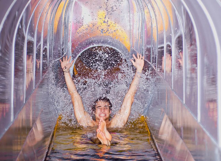 Junger Mann rutscht jubelnd eine Wasserrutsche in einer Erlebnistherme in Süddeutschland hinunter